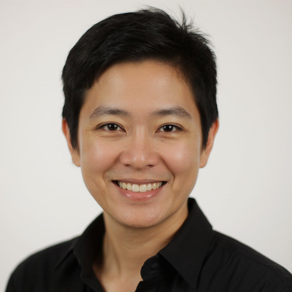 A person with short black hair, wearing a black collared shirt, smiling at the camera against a plain white background.